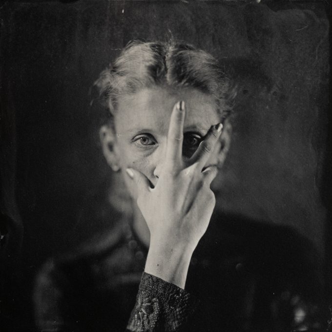 Black-and-white portrait of a person with intense eye contact, framed in classic wet plate collodion style, capturing fine details and organic textures. Schwarz-Weiß-Porträt einer Person mit intensivem Blickkontakt, im klassischen Nassplatten-Kollodium-Stil, der feine Details und organische Texturen einfängt.